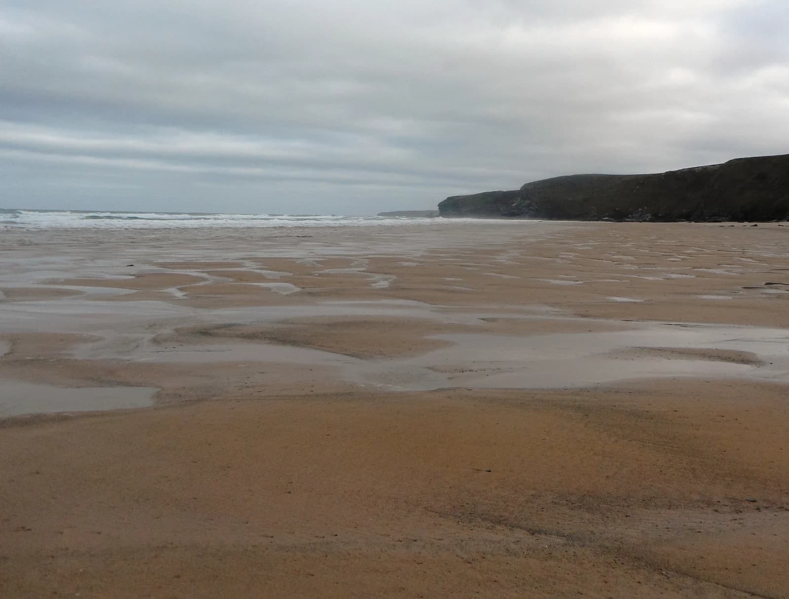 Wide wet sand at low tide on Watergate Bay beach near Newquay, with the cliffs running north