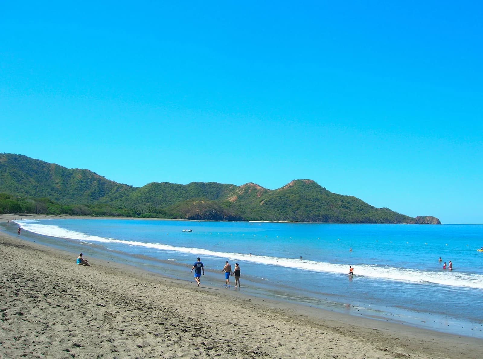 Families walking and paddling on Playa Matapalo in Guanacaste under a clear sky