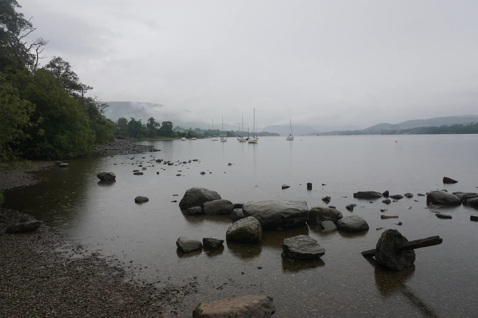 Rocks along the shore of Ullswater near Pooley Bridge, with yachts moored on the calm water