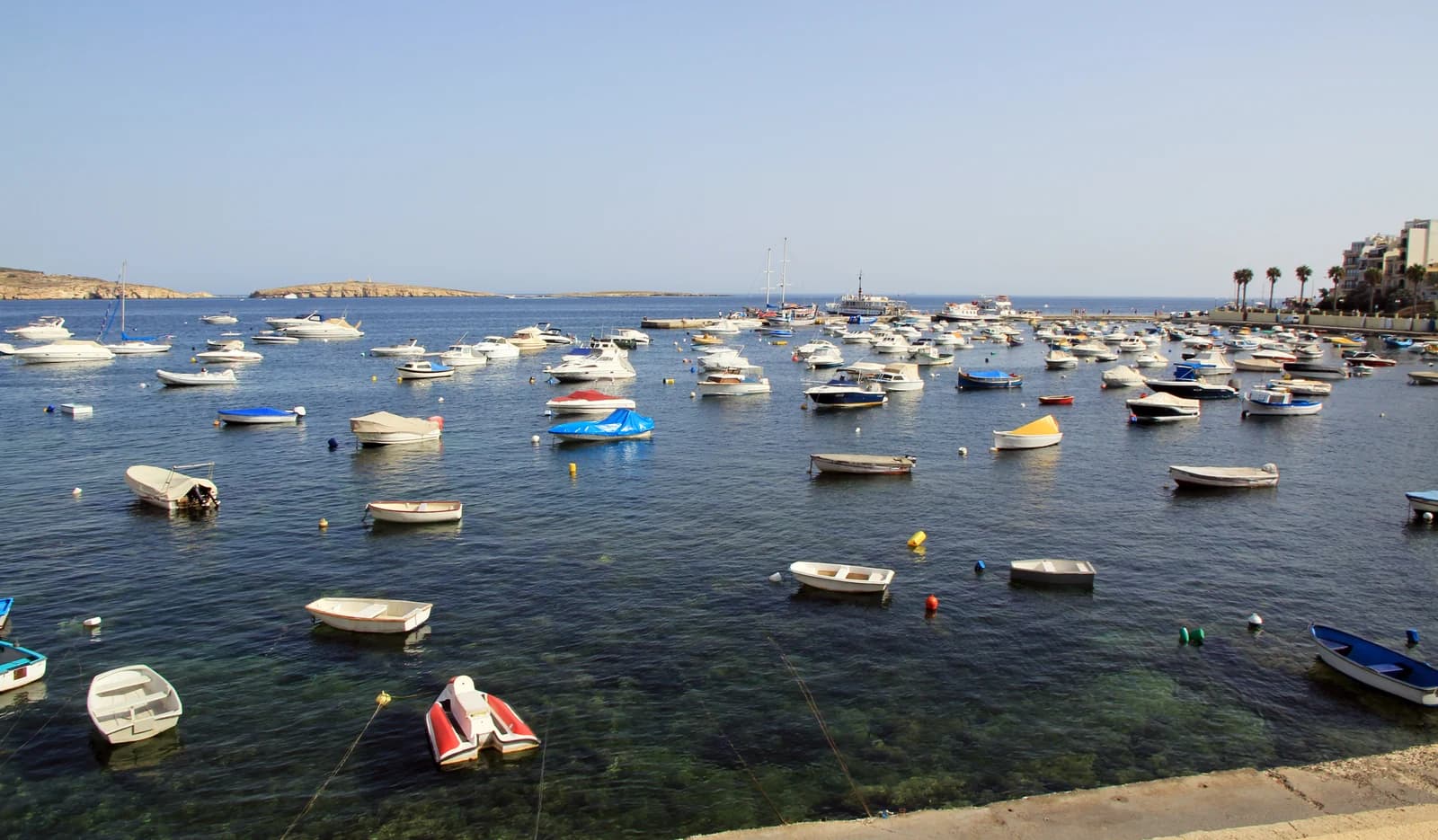 Small boats moored in the clear water of the harbour at Buġibba