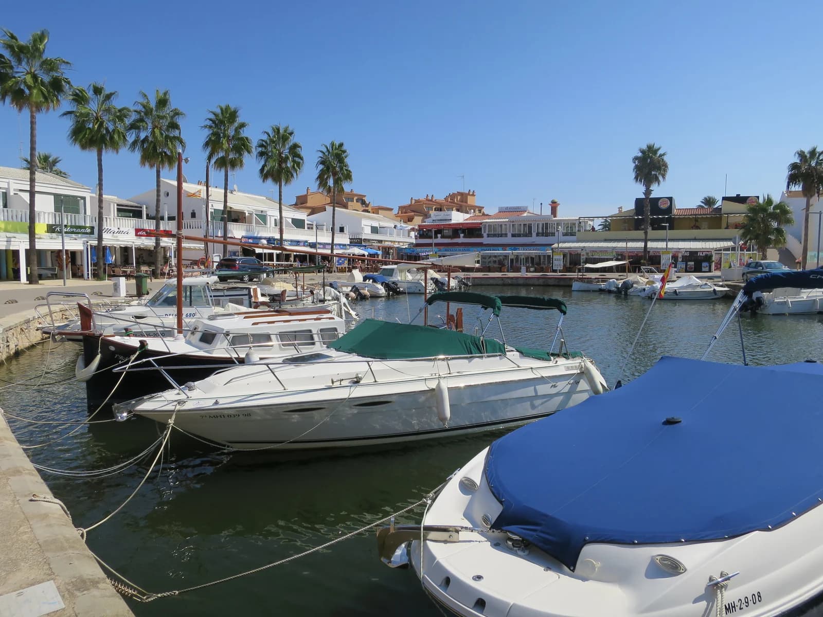 Motorboats moored along the quay in front of the restaurants at Cala'n Bosch marina