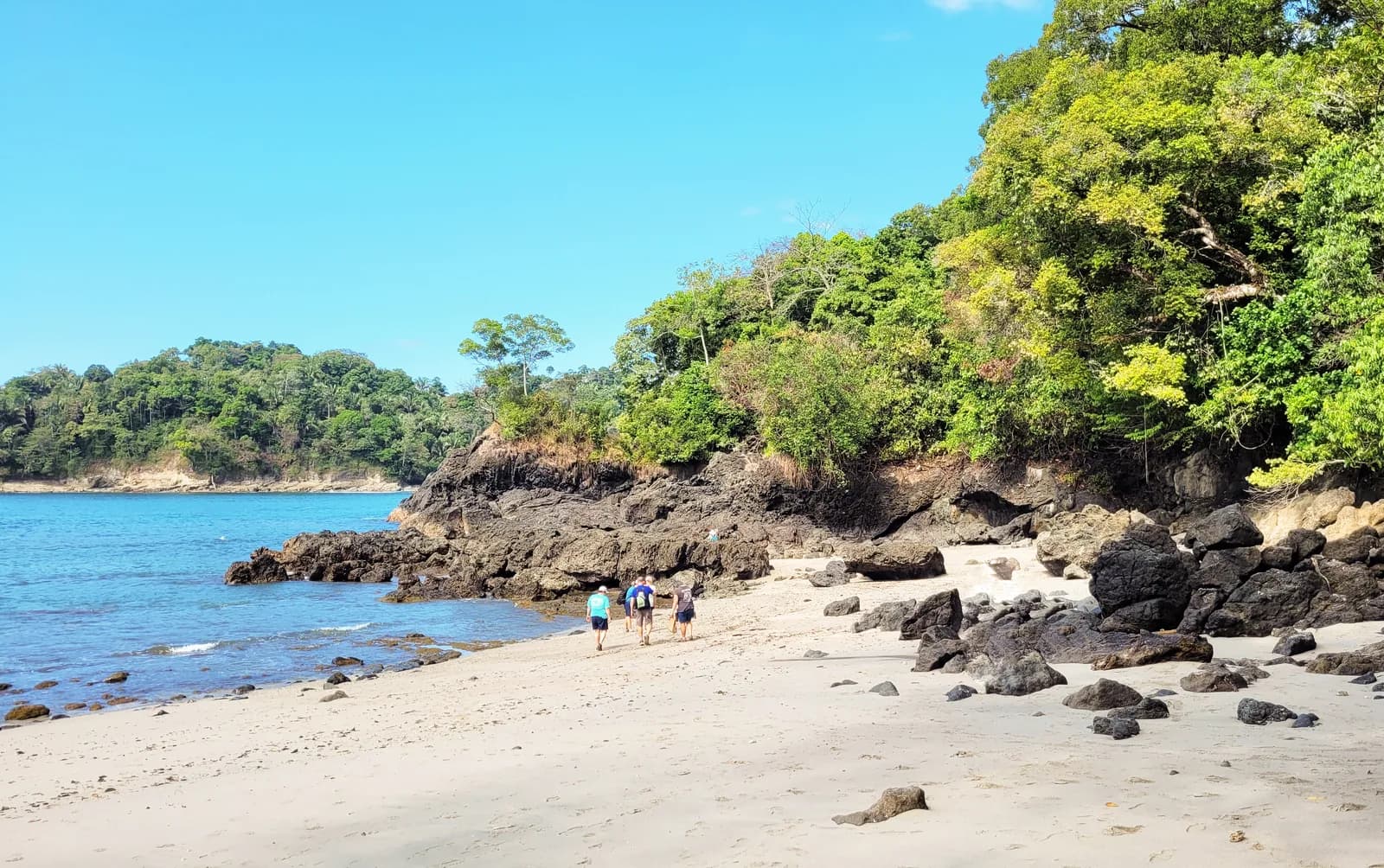 A white-sand beach inside Manuel Antonio National Park backed by rainforest and dark volcanic rocks