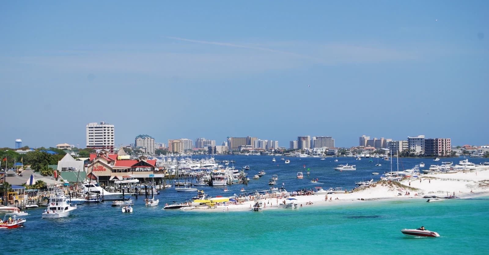 Destin Harbor in Florida, with boats moored along the quay, the condominium skyline behind and the sandbar in the emerald water