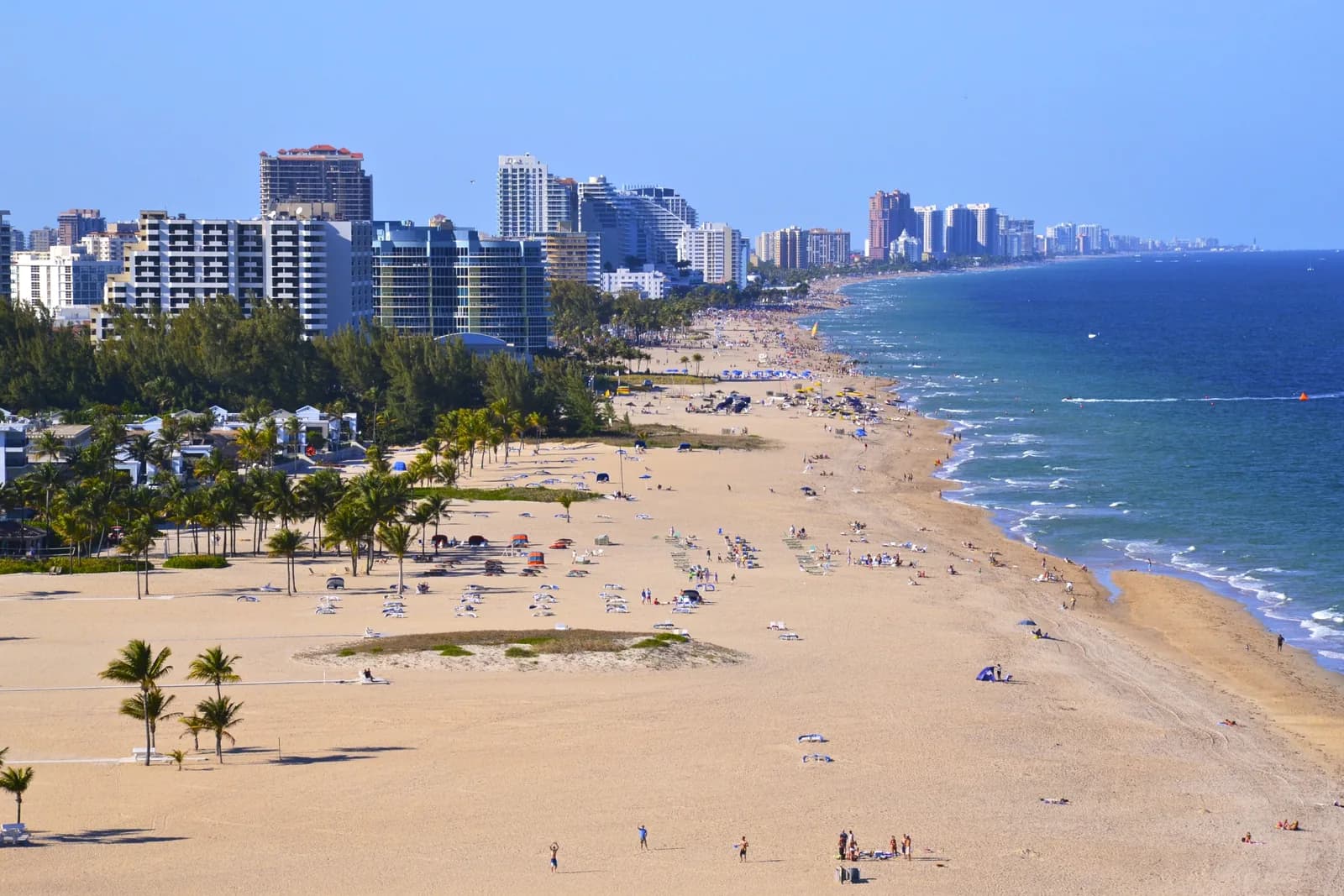 The wide sand of Fort Lauderdale beach from above, with sun loungers, palms and the hotel strip running north