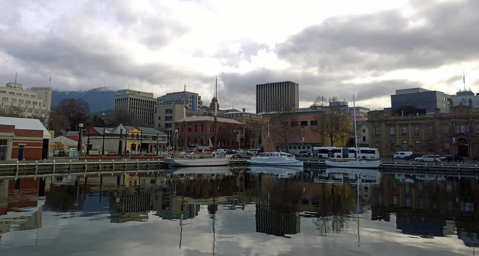 Boats moored along Constitution Dock in Hobart, the waterfront buildings reflected in the water under cloud