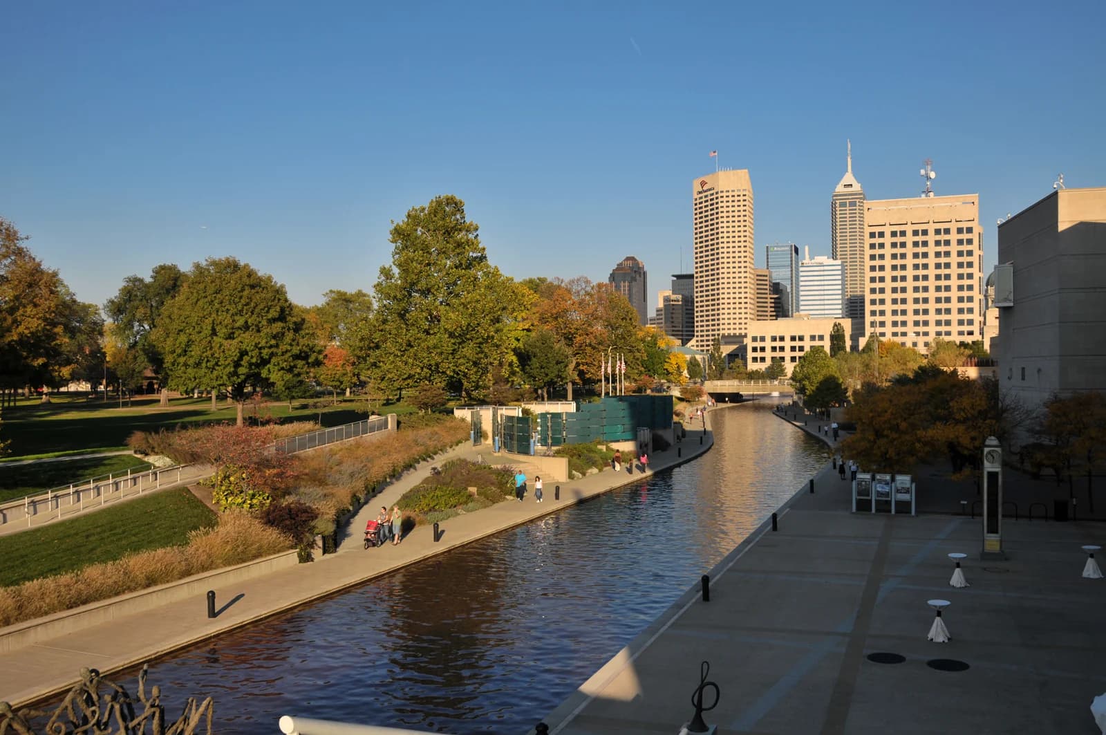 The Indianapolis downtown canal in evening light, with walkers on the promenade and the skyline behind