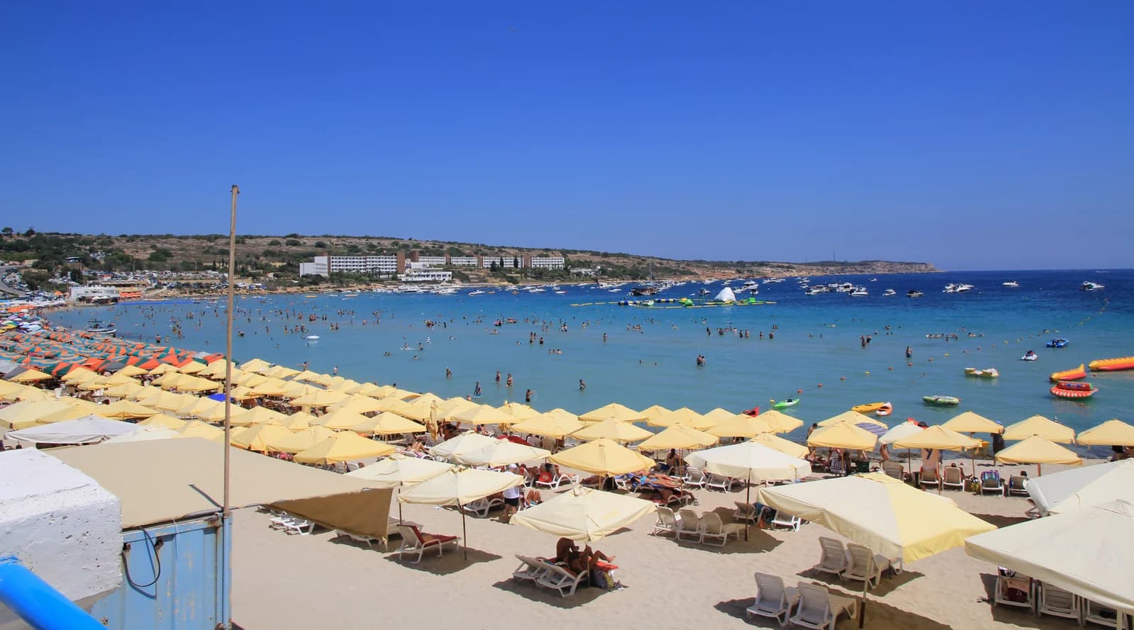 Umbrellas and sunbeds on the sand at Mellieħa Bay, with swimmers in the shallow water
