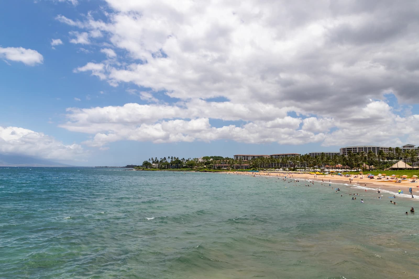 The curve of Wailea beach on Maui seen from the water, with low resort buildings and palms along the shore