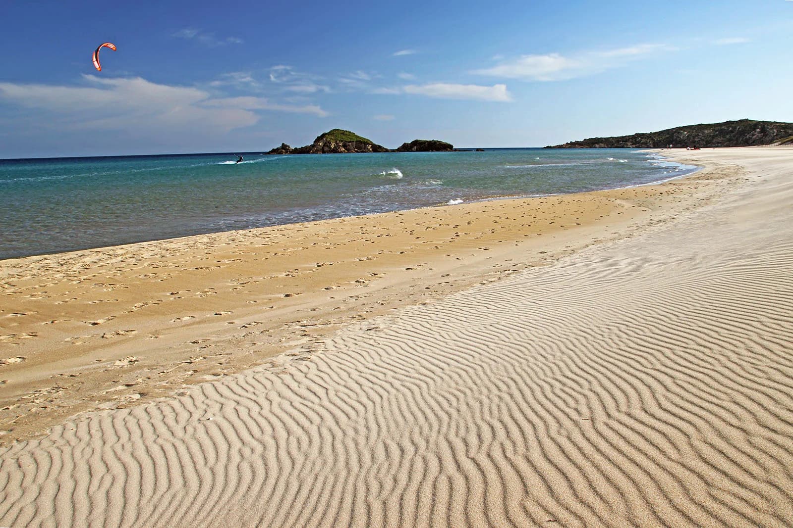 Rippled sand and shallow turquoise water at Su Giudeu beach in Chia, southern Sardinia