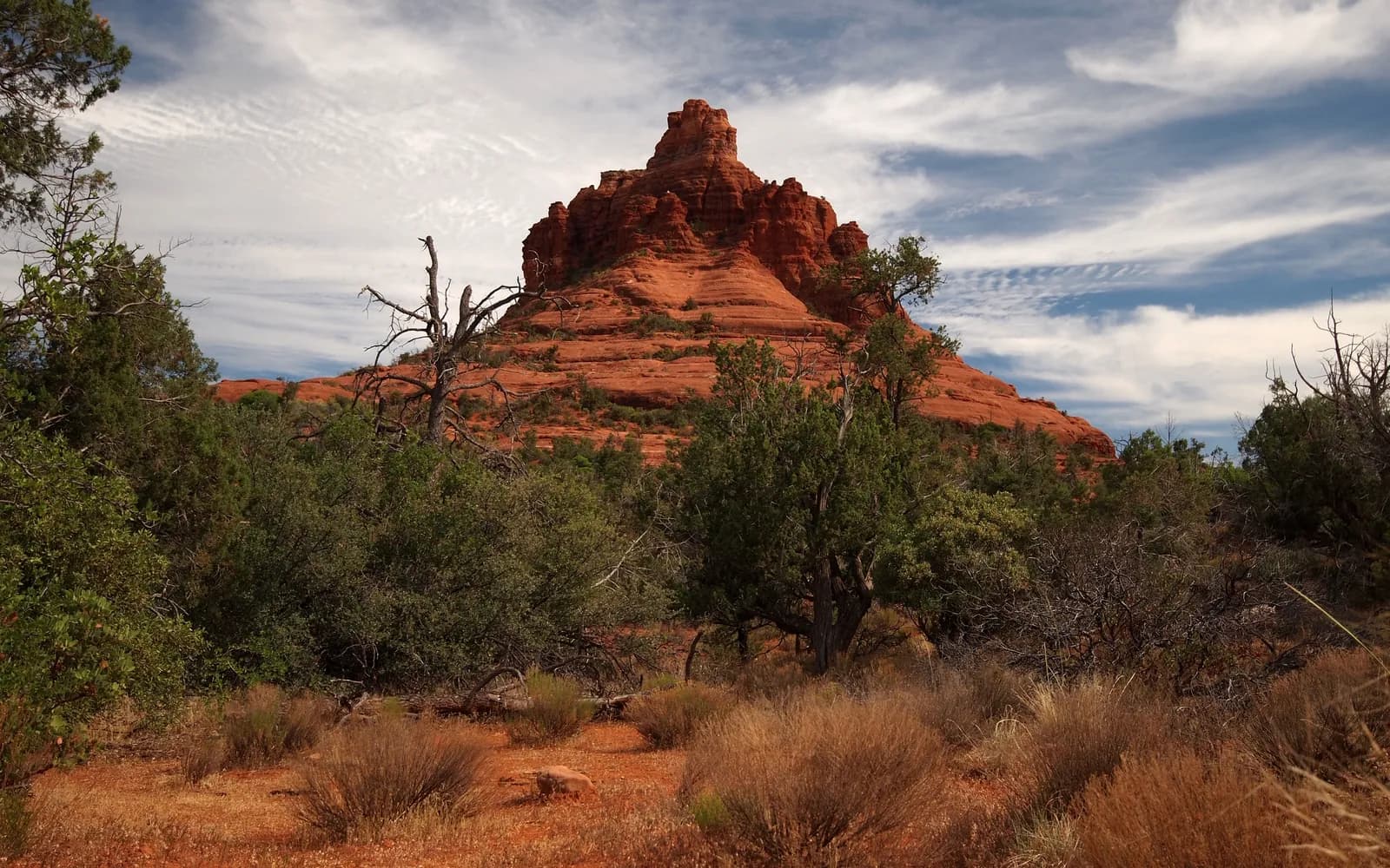Bell Rock rising above juniper and red earth outside Sedona under a cloud-streaked sky