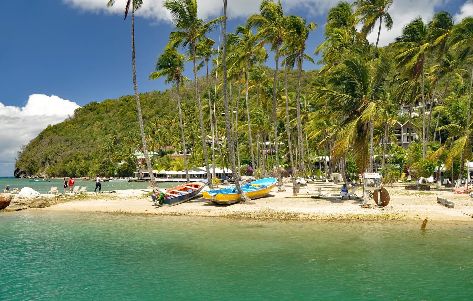 Palms leaning over the sand at Marigot Bay in Saint Lucia, with small boats drawn up and green hills behind