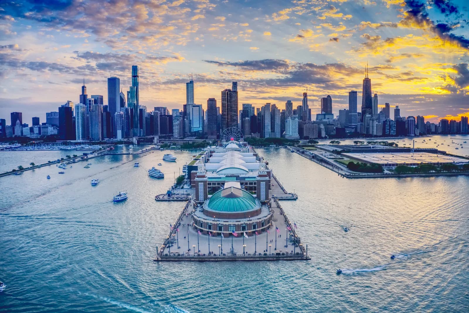 Navy Pier reaching into Lake Michigan at sunset, with tour boats on the water and the Chicago skyline behind