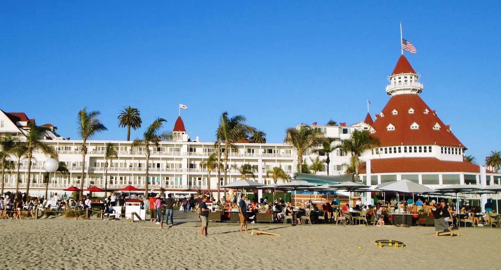 The long white frontage and red turret of the Hotel del Coronado seen from the beach in San Diego