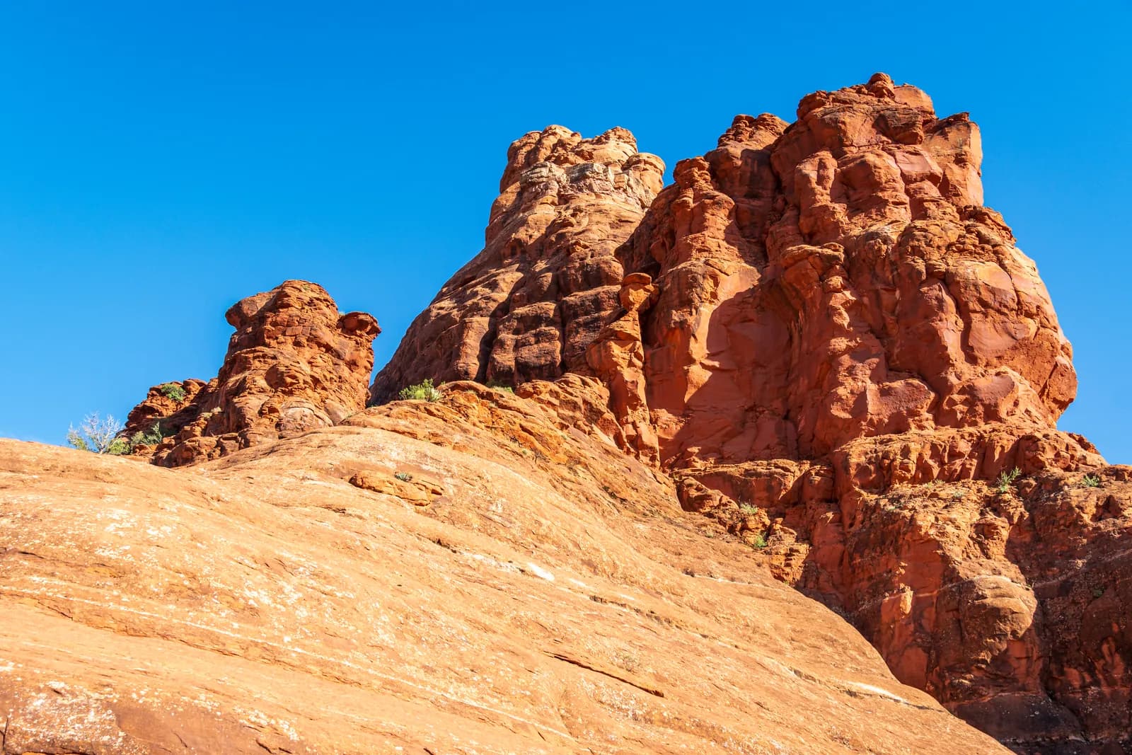 Weathered red sandstone formations above pale slickrock under a deep blue sky near Bell Rock in Sedona