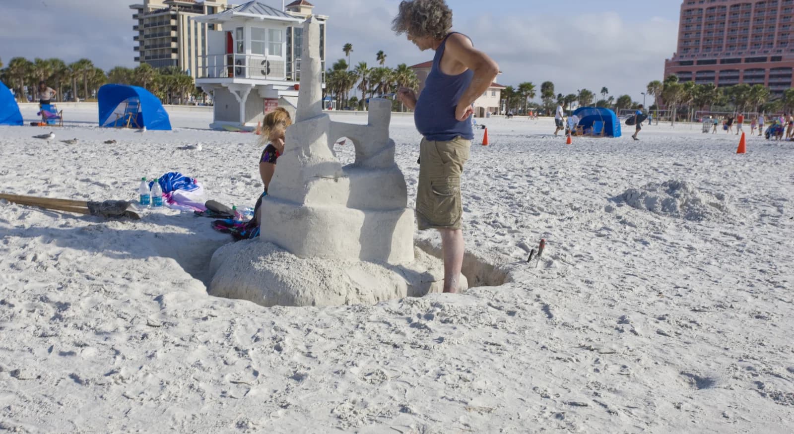 A child building a sandcastle on the white sand at Clearwater Beach, with a lifeguard tower and beach resorts behind