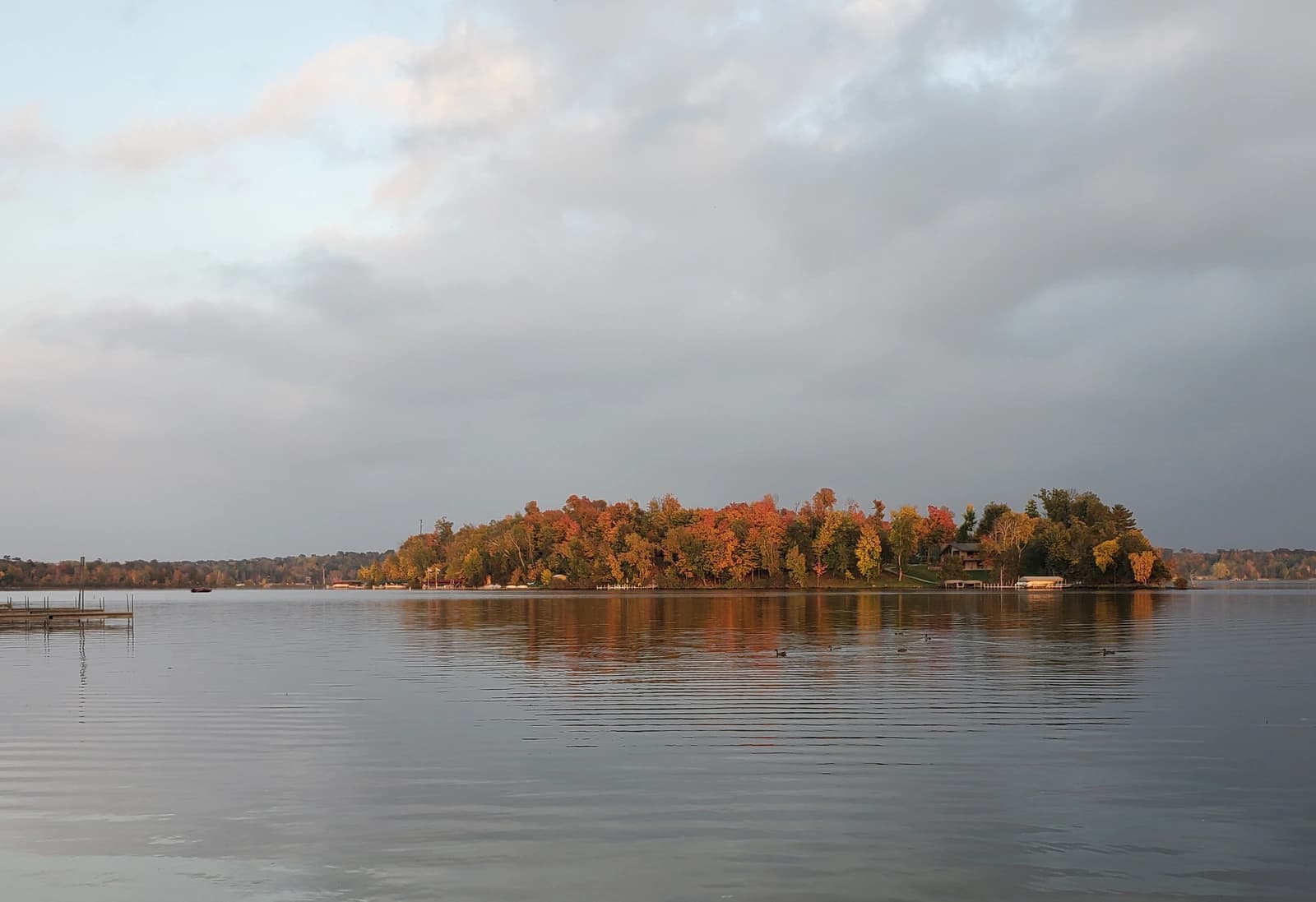 Autumn colour on the wooded island in East Gull Lake, Minnesota, seen across calm water at sunset
