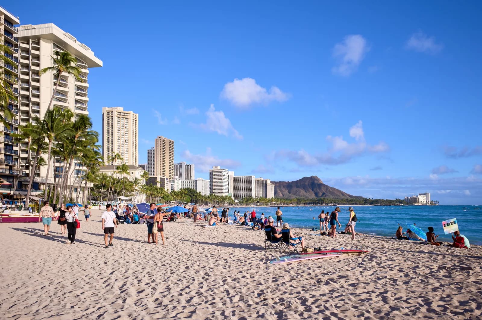 Waikiki Beach on a clear afternoon, with hotel towers and palms along the sand and Diamond Head rising at the far end