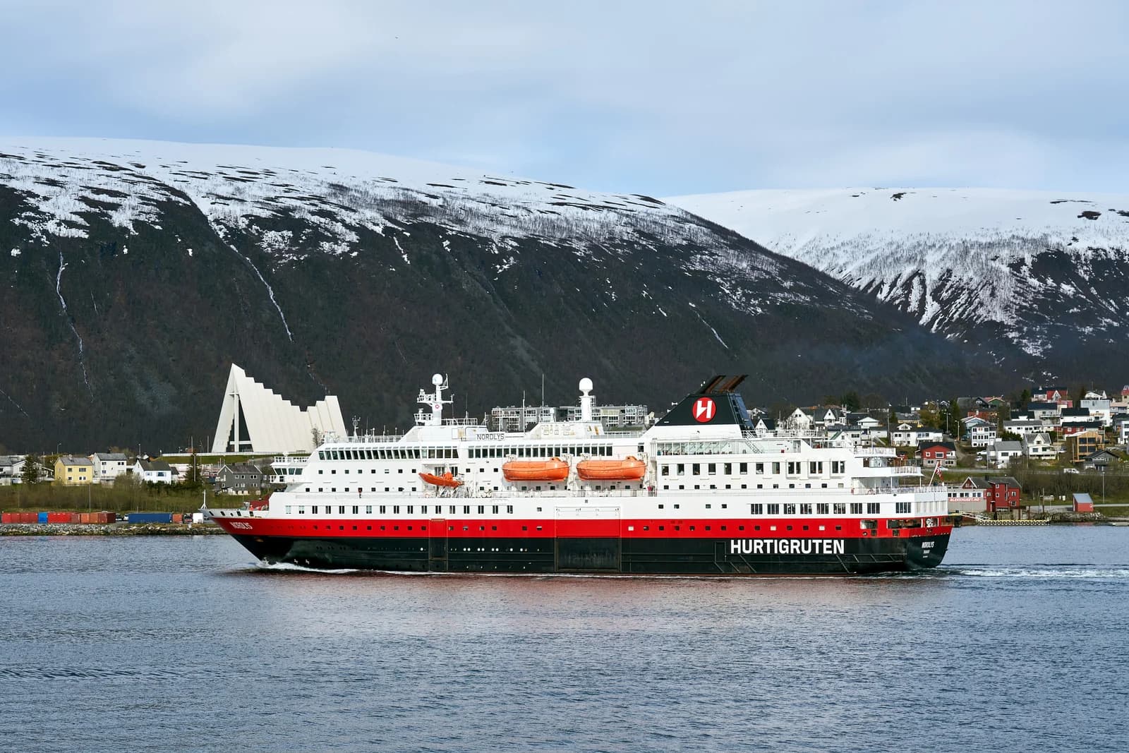 A coastal ship passing below the Arctic Cathedral at Tromsdalen, the Tromso bridge crossing the water behind it