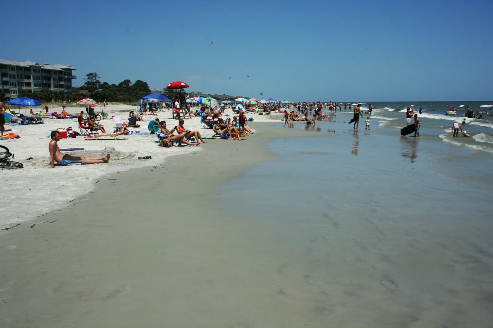 Sunbathers, umbrellas and swimmers along a wide, flat beach on Hilton Head Island on a clear summer day