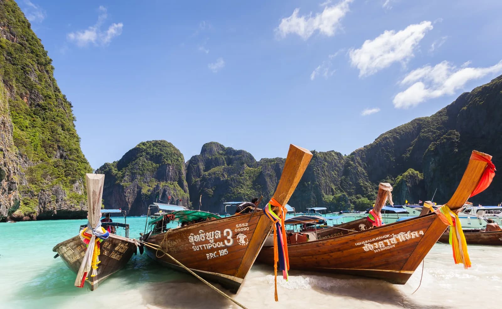 Colorful longtail boats on turquoise water at Maya Bay, Ko Phi Phi Leh, Thailand, with limestone cliffs behind