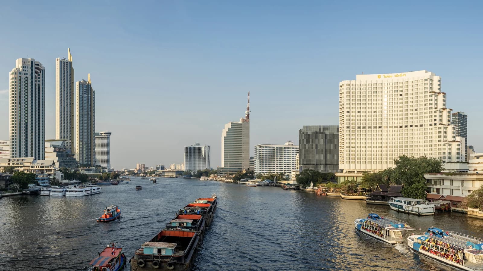 The Chao Phraya river in Bangkok with rice barges, ferries and riverside hotel towers