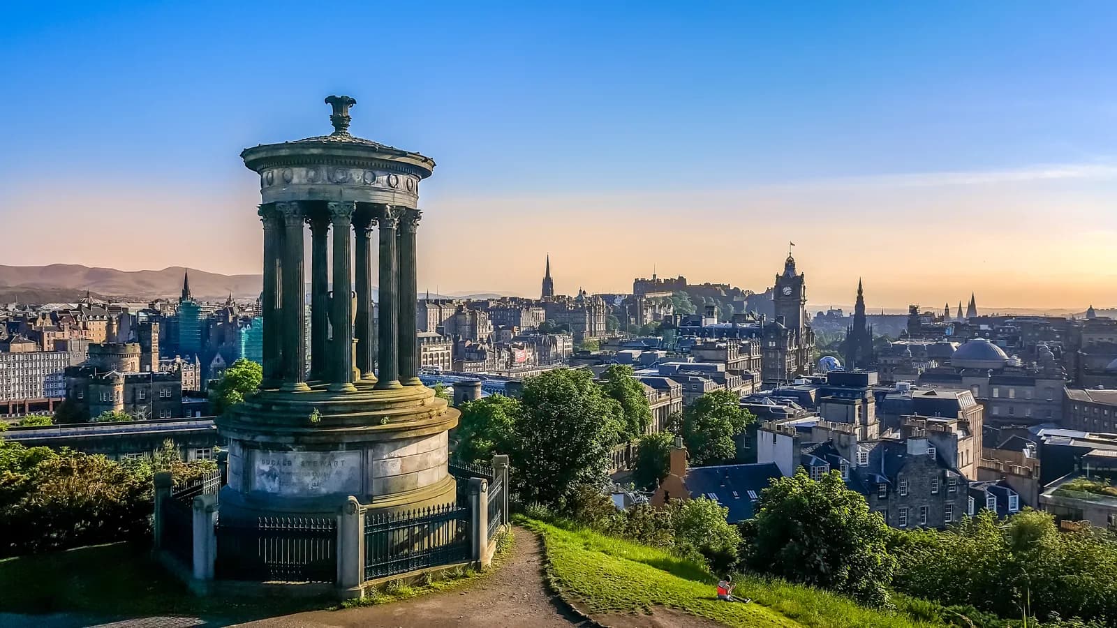 Edinburgh skyline from Calton Hill with the Dugald Stewart Monument in the foreground and the castle and Old Town spires in golden evening light