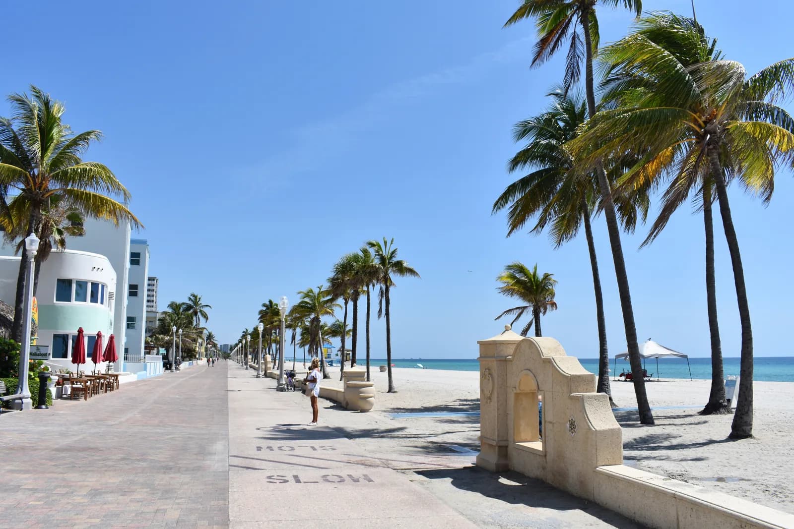 Palms and pastel buildings along the Hollywood Beach Broadwalk in Florida, with the sand and sea to one side