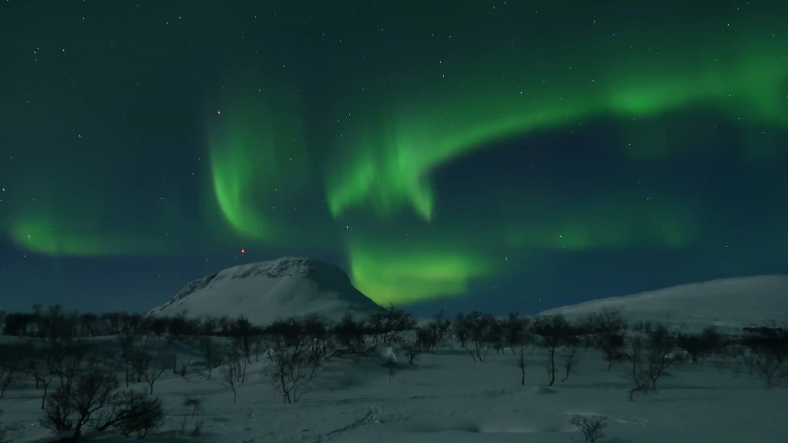 Green aurora arcing over the snow covered slopes of Saana fell at Kilpisjarvi in Finnish Lapland
