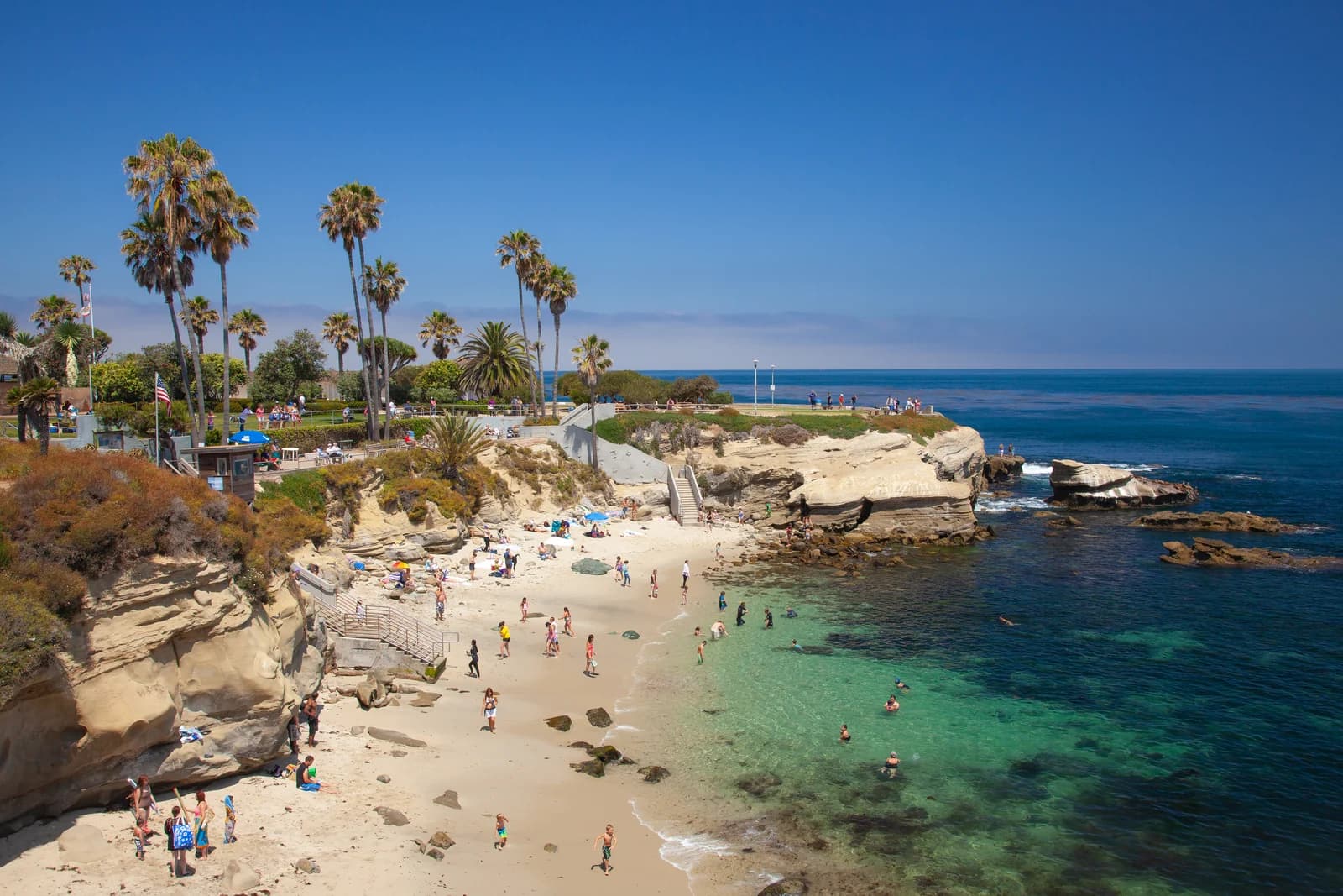 Families on the sand at La Jolla Cove in San Diego, with palms above the cliff and clear turquoise water