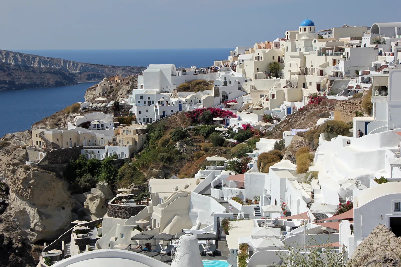 Whitewashed hotels and houses of Oia village stacked down Santorini's caldera cliff, with a blue-domed church above the Aegean Sea