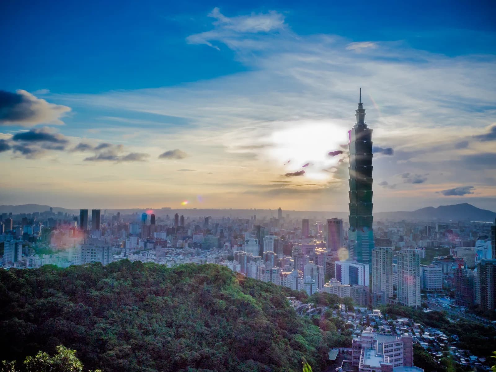 Taipei 101 rising above the city at sunset, seen across the wooded hills