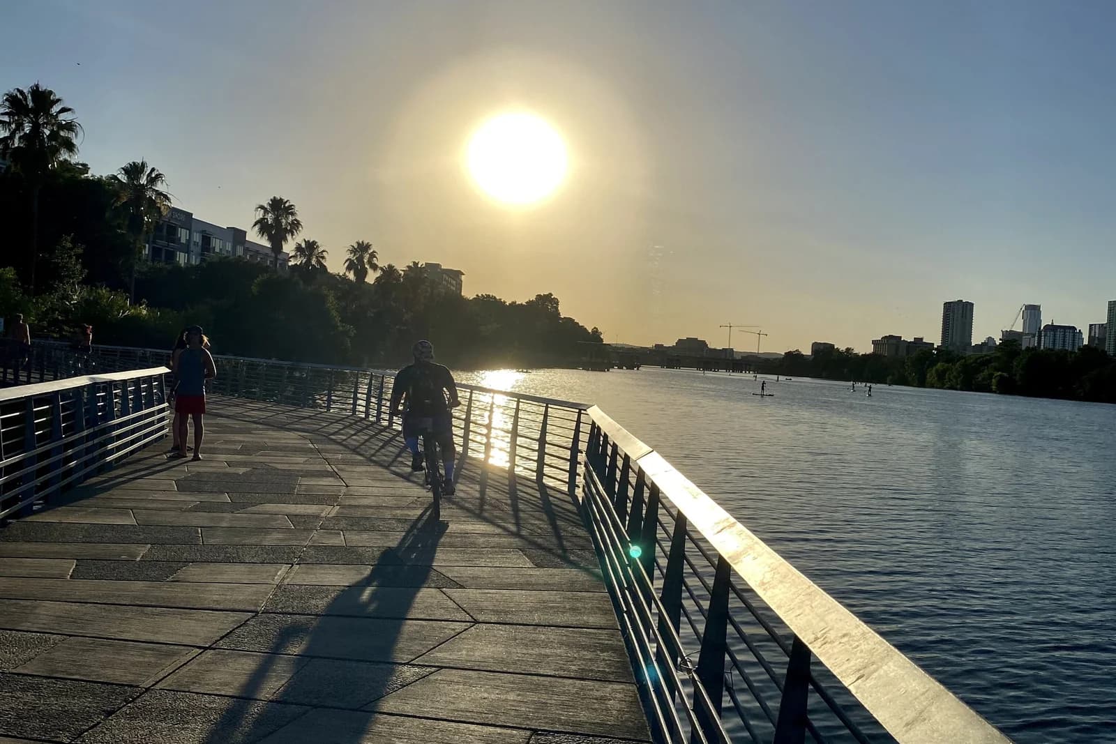 Walkers and a cyclist on the boardwalk section of the Butler Trail out over Lady Bird Lake at sunset
