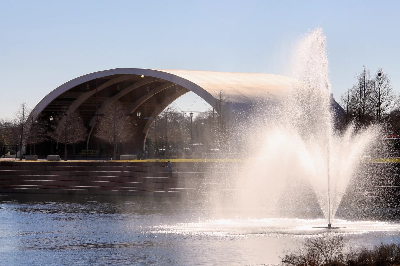 The fountain on Mueller Lake with the curved roof of the Browning Hangar behind it