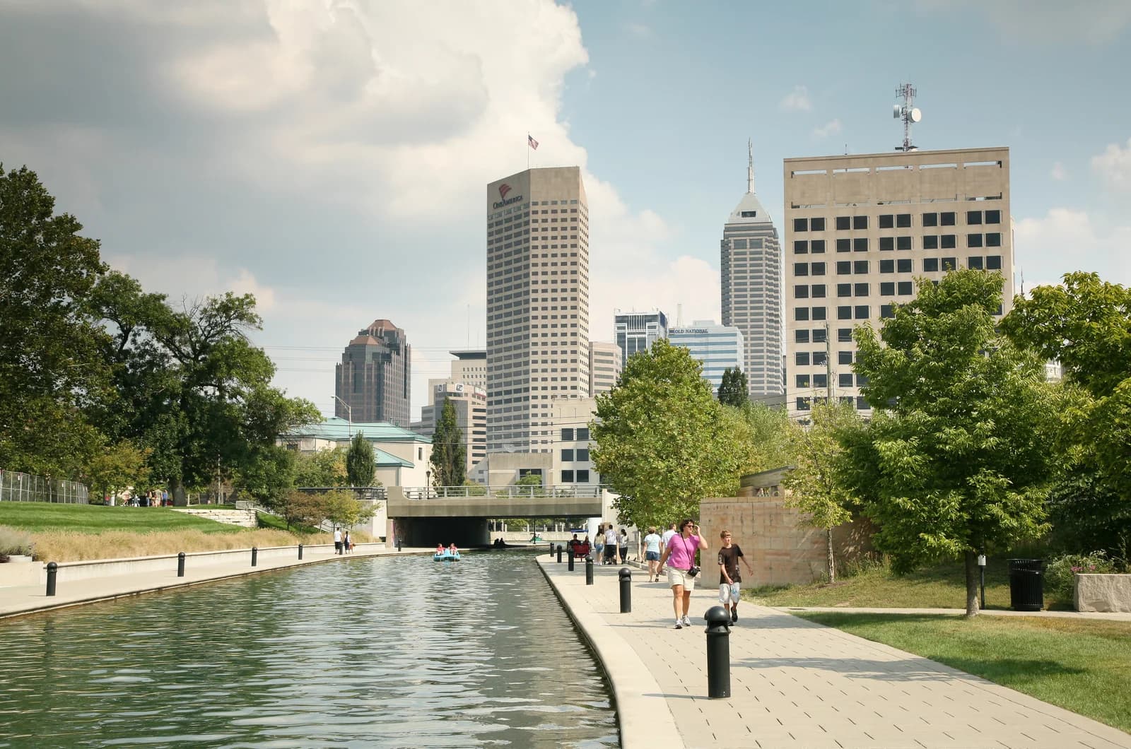 Walkers on the paved Indianapolis Canal Walk with the downtown skyline rising behind the water