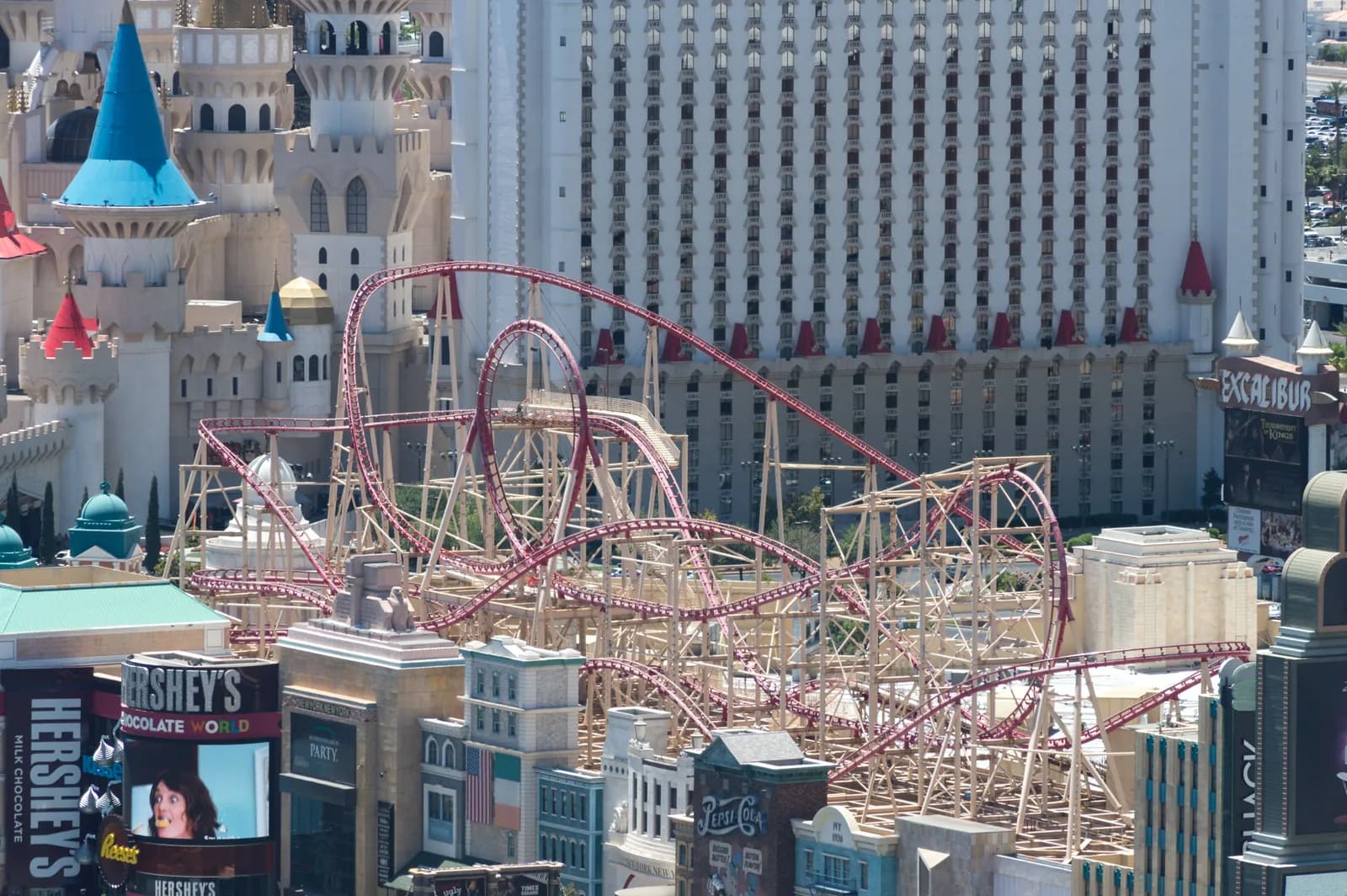 The red track of the Big Apple Coaster looping above the New York-New York facades, with the Excalibur towers behind