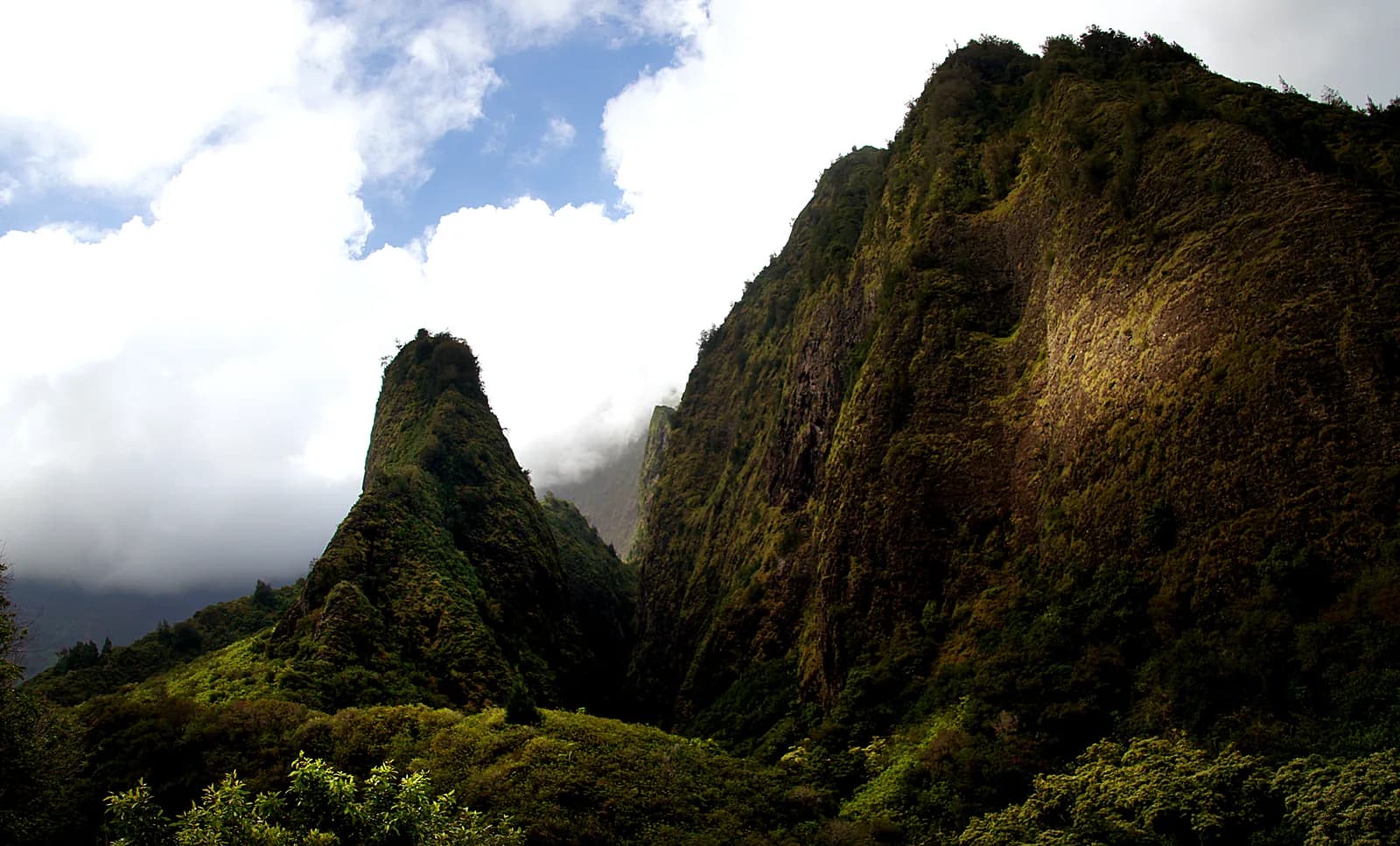 The Iao Needle rising from the forested walls of Iao Valley on Maui, with cloud spilling through the gap behind it