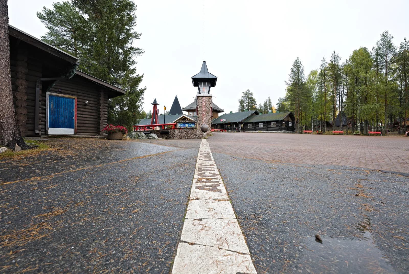 The Arctic Circle marker line at Santa Claus Village outside Rovaniemi, painted across the ground between the timber buildings