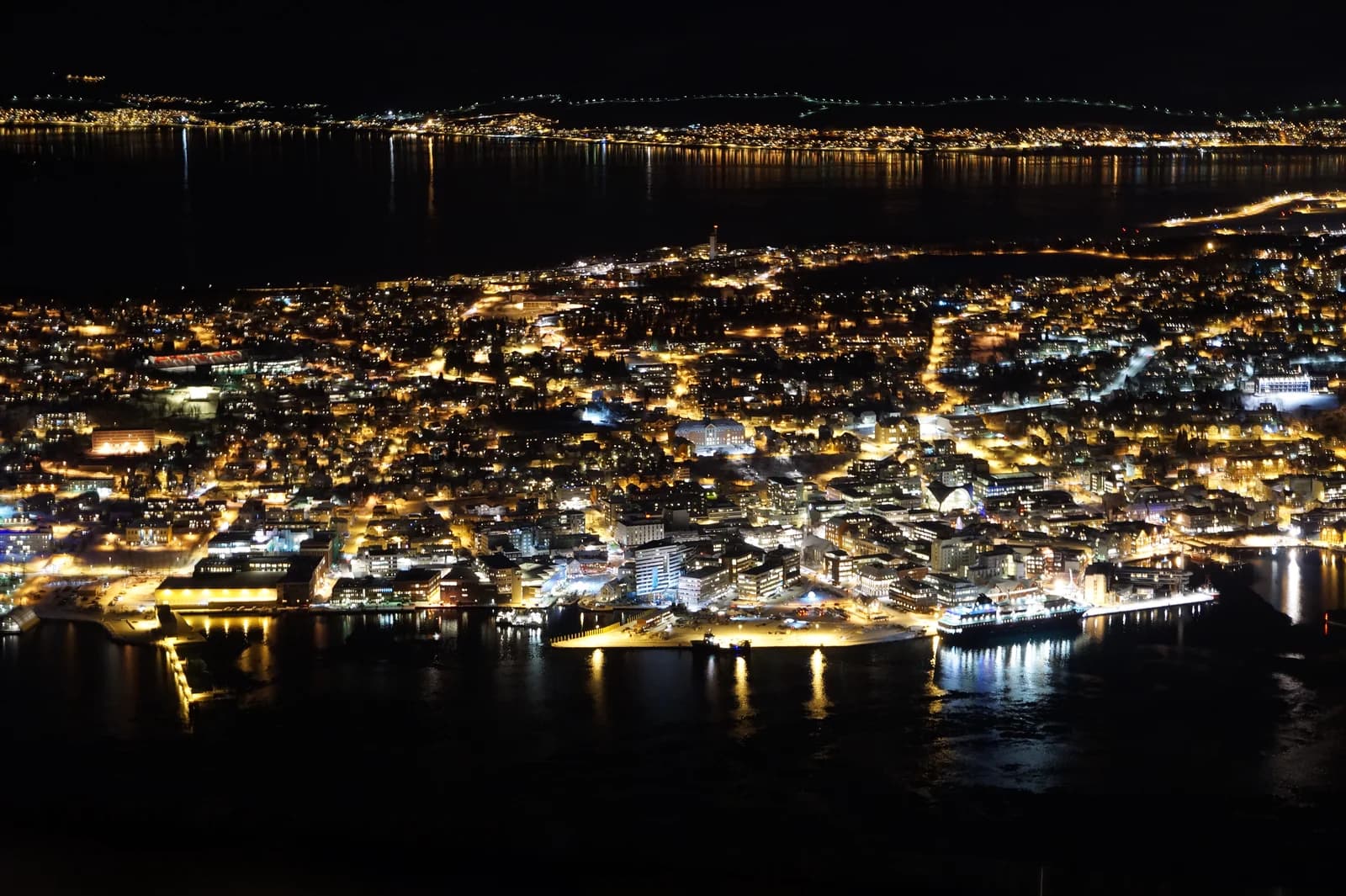 Snow-covered Tromso and its bridge seen from the mountain above on a December afternoon, already dark blue at half past three
